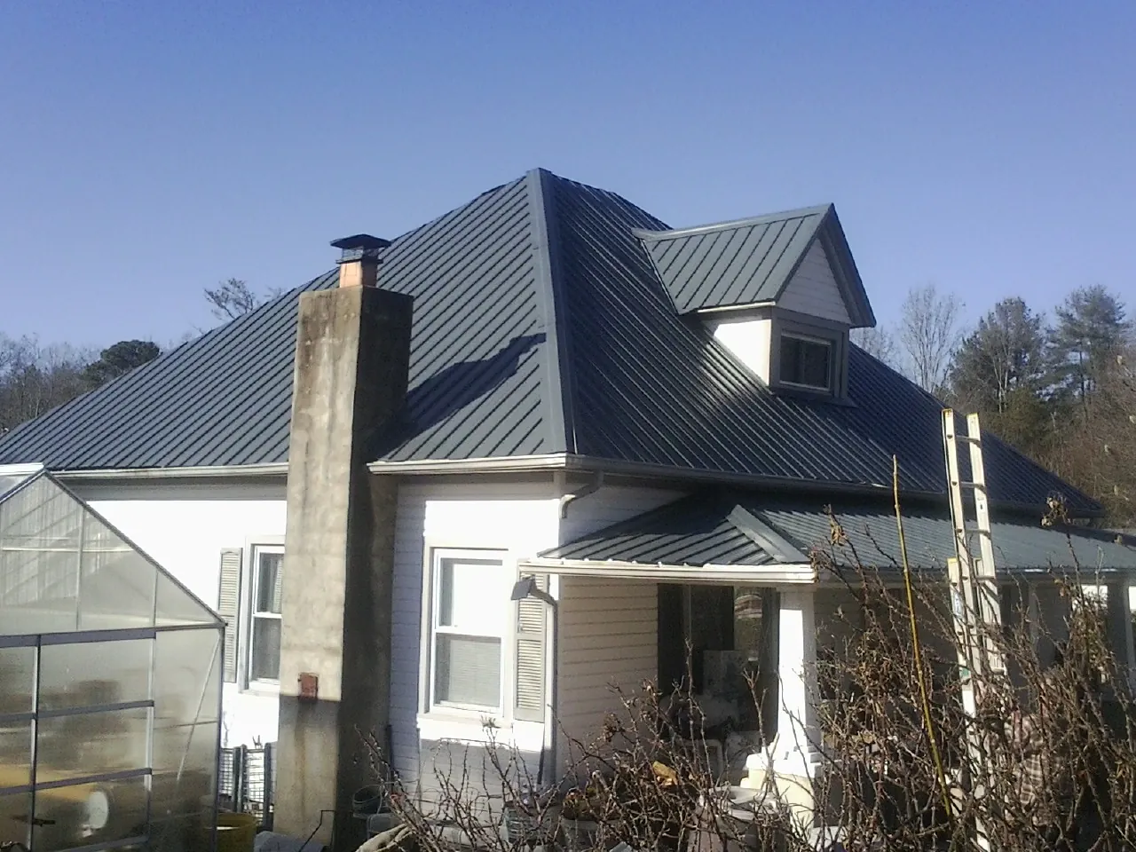 Dark blue standing seam metal roof on a white farmhouse with dormer — Slate & Tile Roof Repair by Roofing Brothers in Lake Ozark