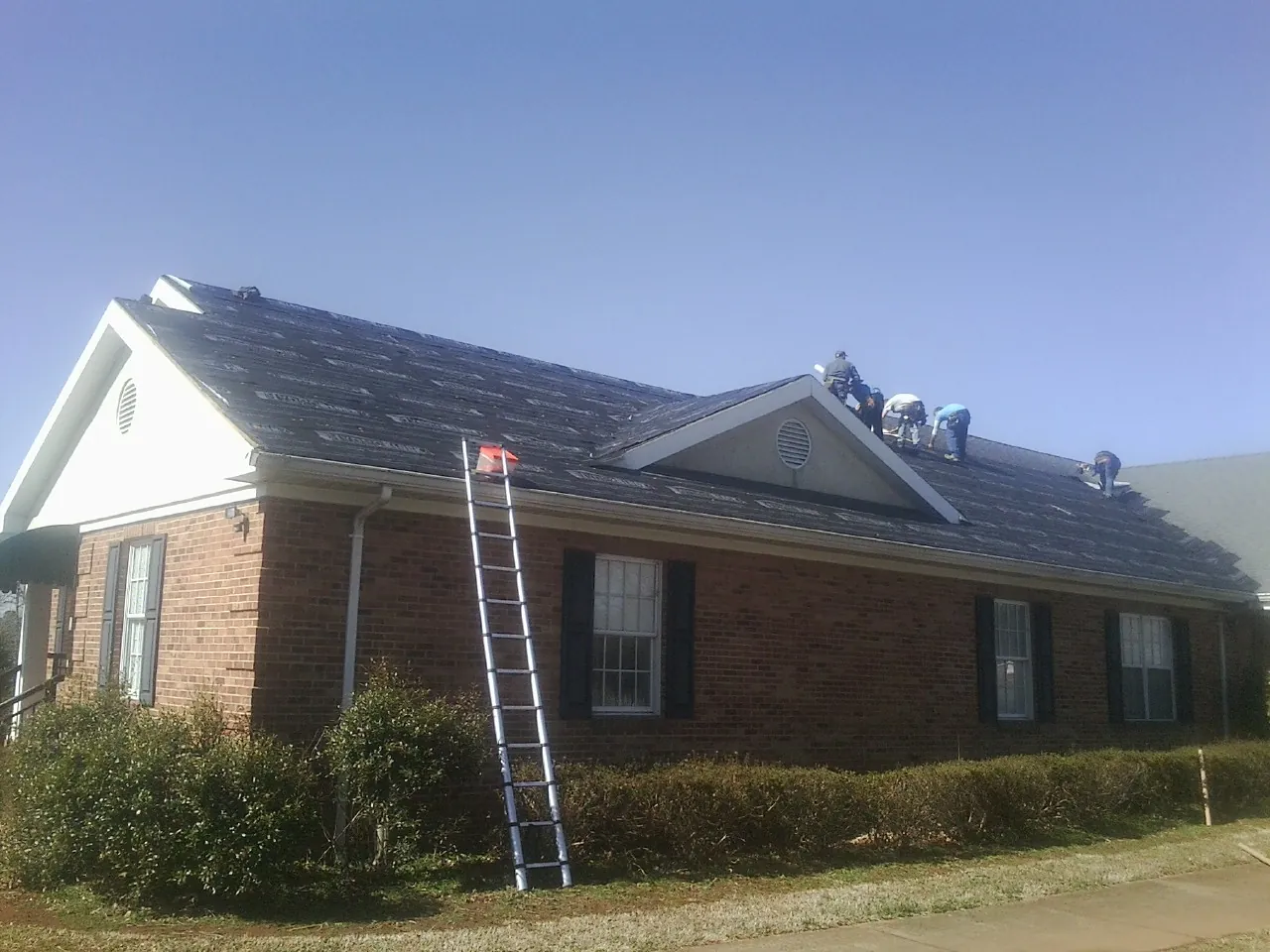Crew tearing shingles off a brick ranch roof with a ladder set — Emergency Roof Repair work by our crew in Lake Ozark