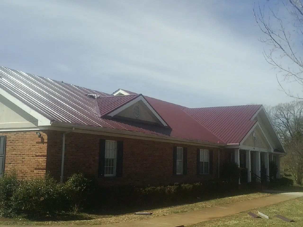 Red metal roof with gabled entries on a long brick building, from a Hail Damage Roof Repair job in Lake Ozark