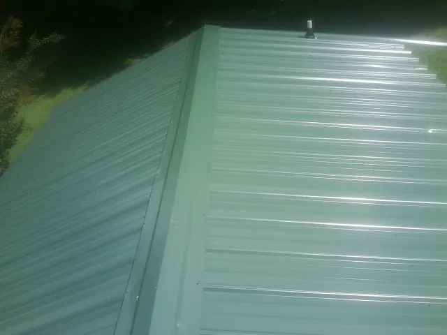 New green metal panels meeting at the ridge of a roof — Flat Roof Repair work by our crew in Lake Ozark