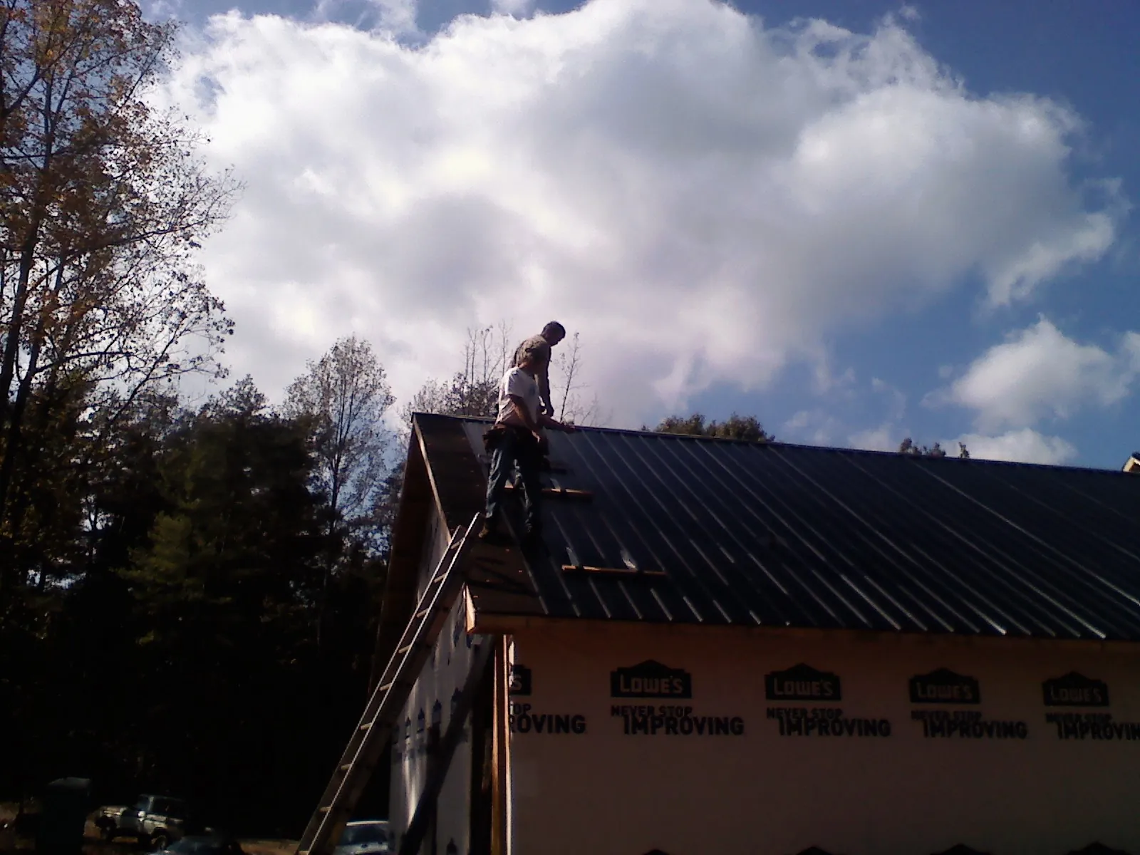 Roofer fastening dark metal panels high against a cloudy sky, from a Roof Inspection job in Lake Ozark