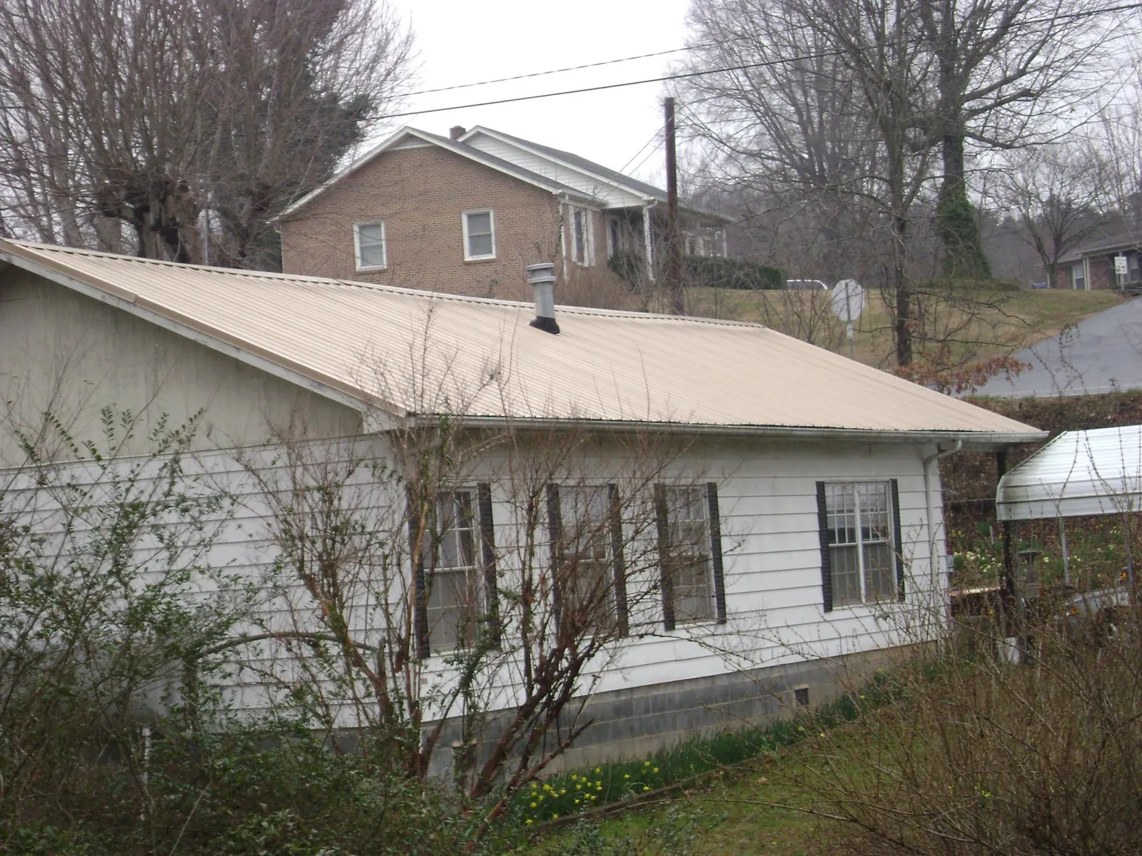 Tan metal roof on a white sided house set into a hillside — Commercial Roofing by Roofing Brothers in Lake Ozark