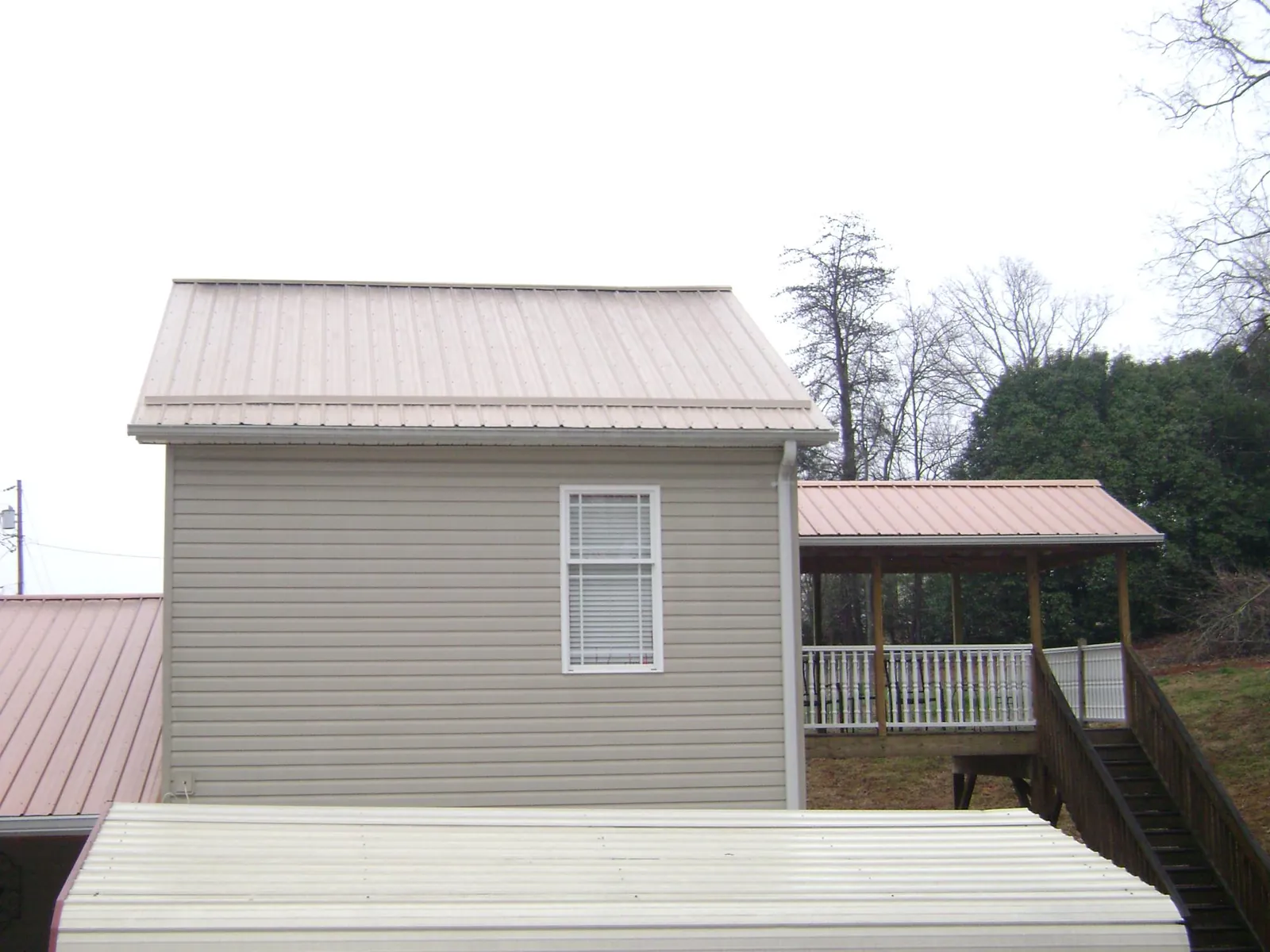 Tan metal roofs on a two story addition and attached porch, from a Roof Replacement job in Lake Ozark